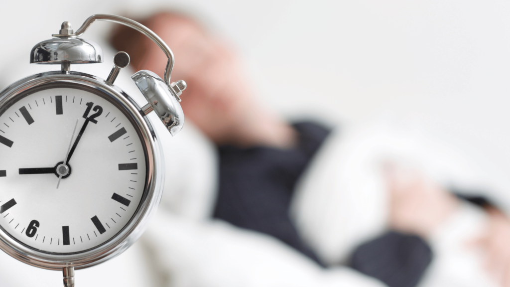 A man sleeping with clock a side of his bed